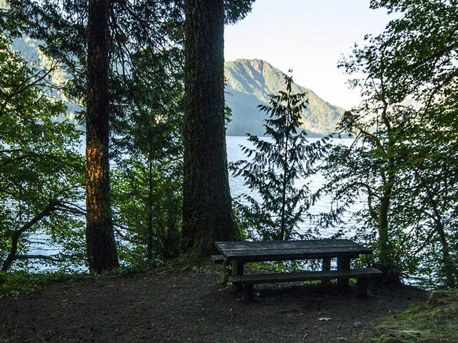 picnic bench at top of hill over body of water with mountain in distance