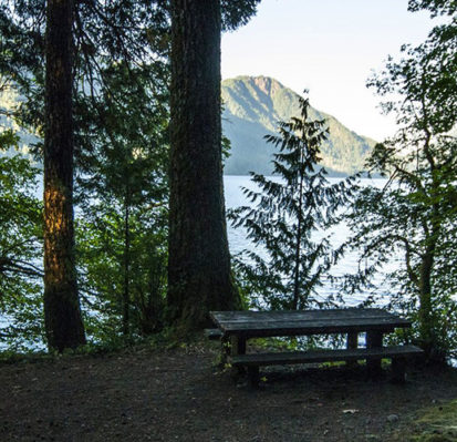 picnic bench at top of hill over body of water with mountain in distance