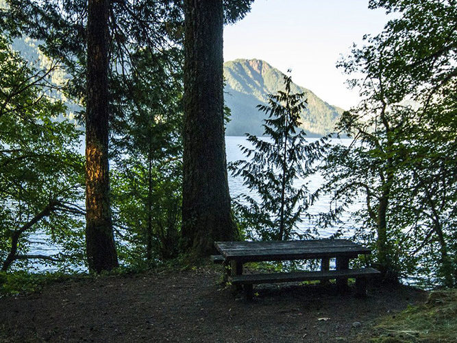 picnic bench at top of hill over body of water with mountain in distance